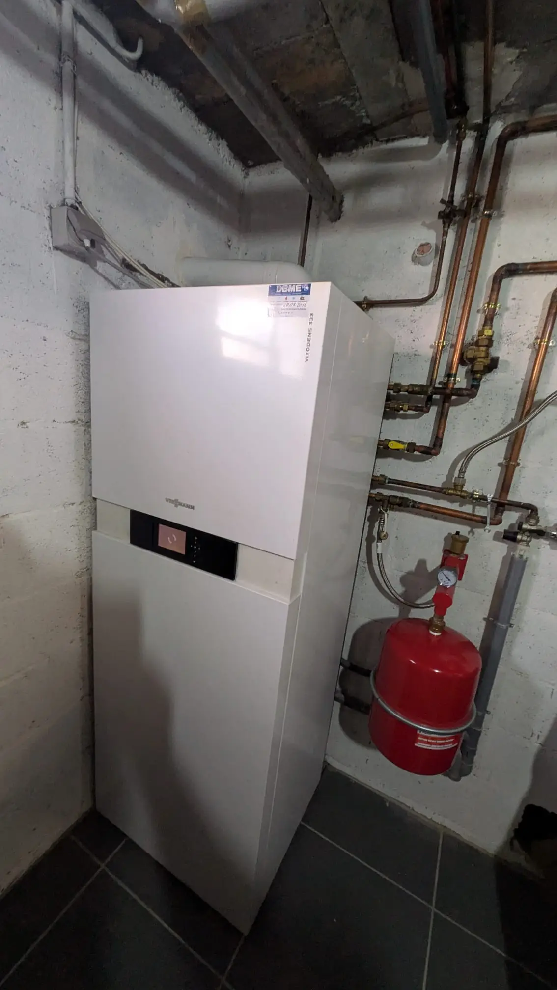 Chaudière gaz à condensation posée au sol dans une chaufferie, raccordée en cuivre, vase d’expansion rouge fixé au mur