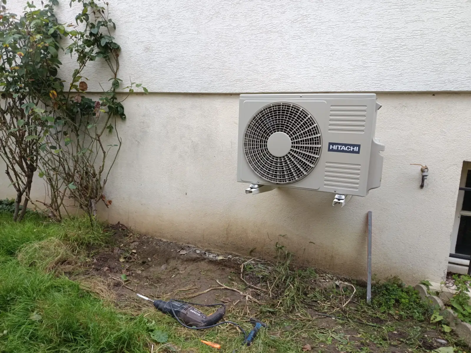 Groupe extérieur de climatisation fixé sur des équerres contre un mur crépi