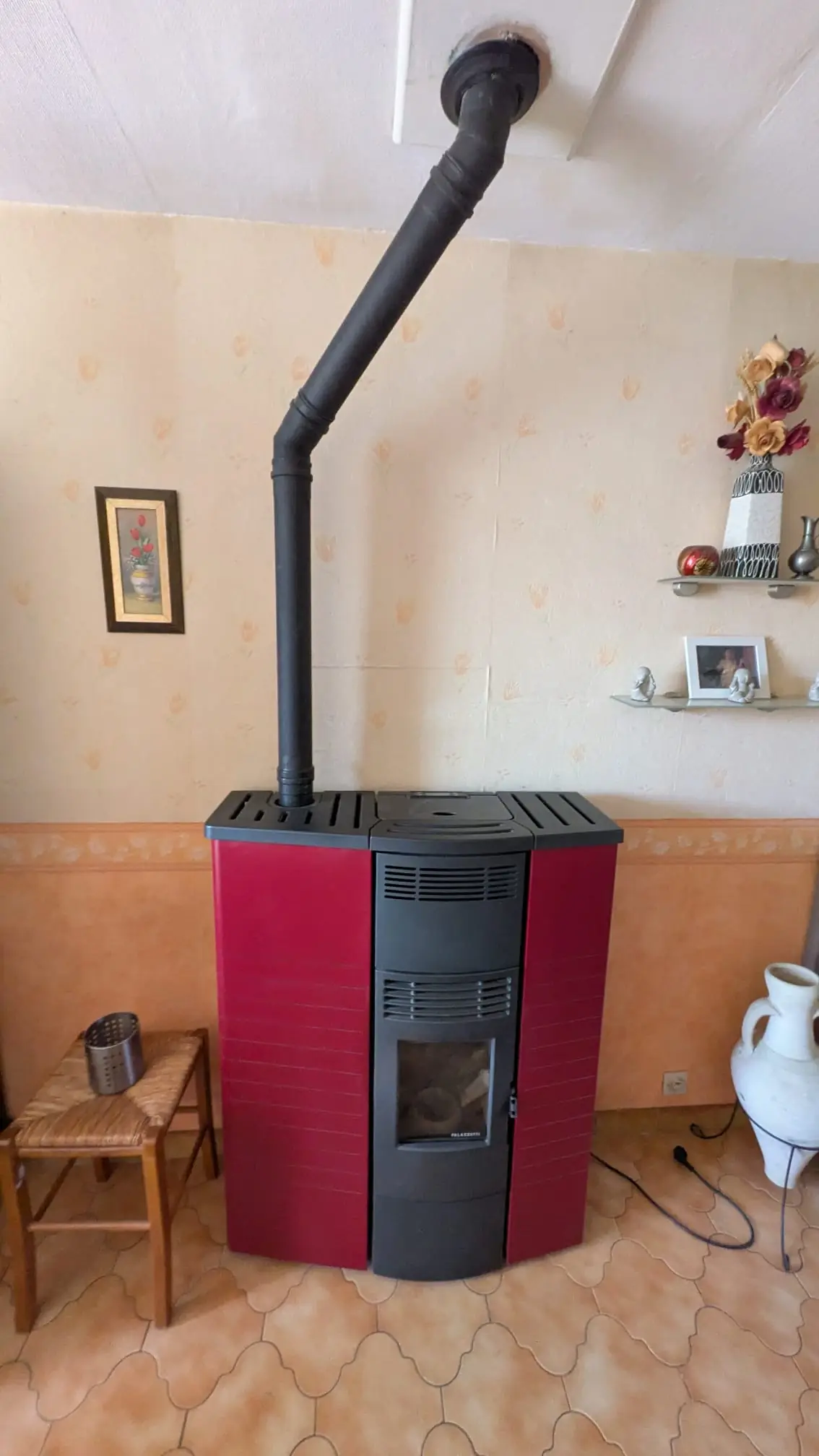 Poêle à granulés rouge installé dans un séjour, conduit coudé raccordé au plafond