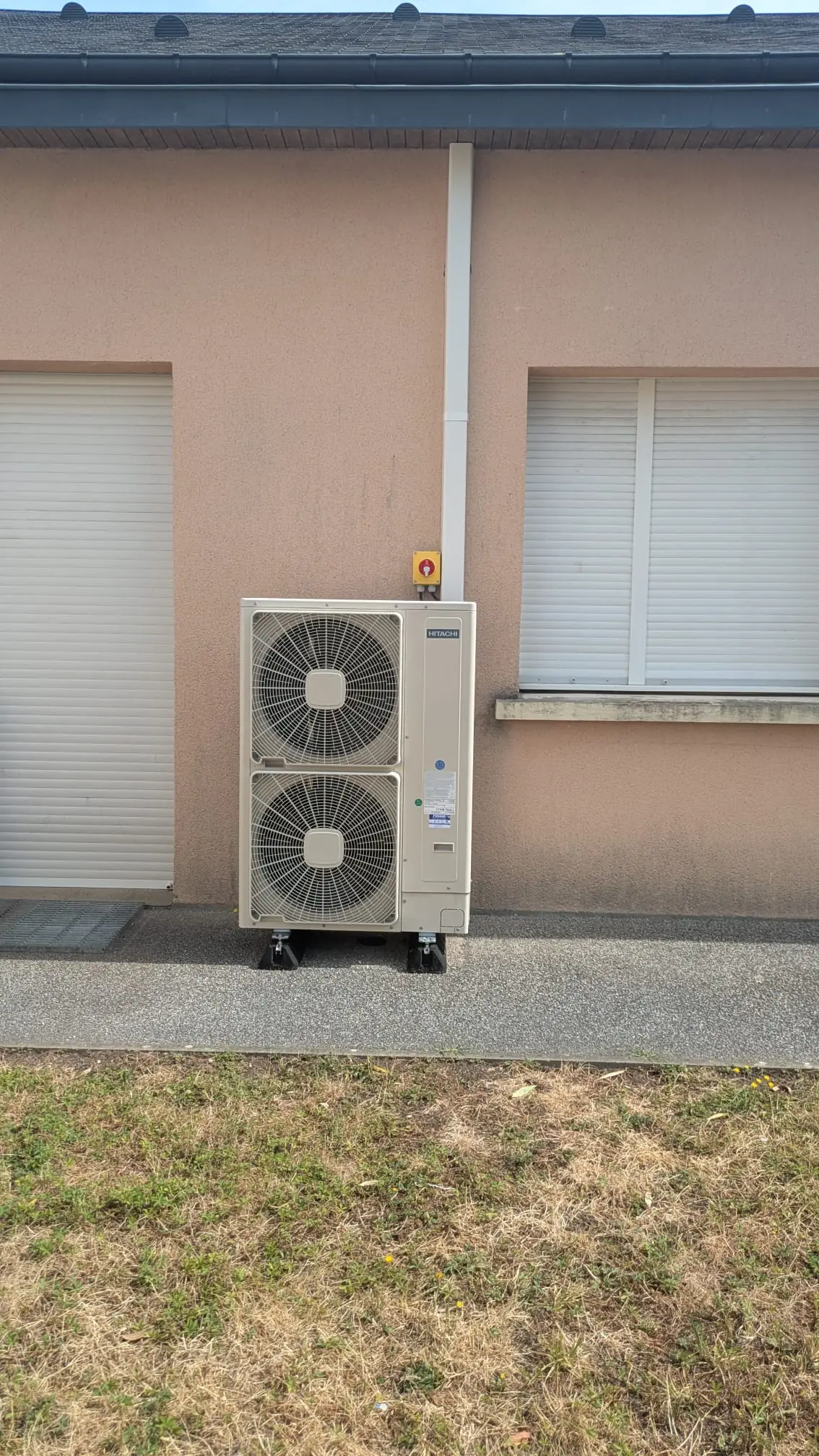 Groupe extérieur de pompe à chaleur à deux ventilateurs, fixé contre une façade crépie